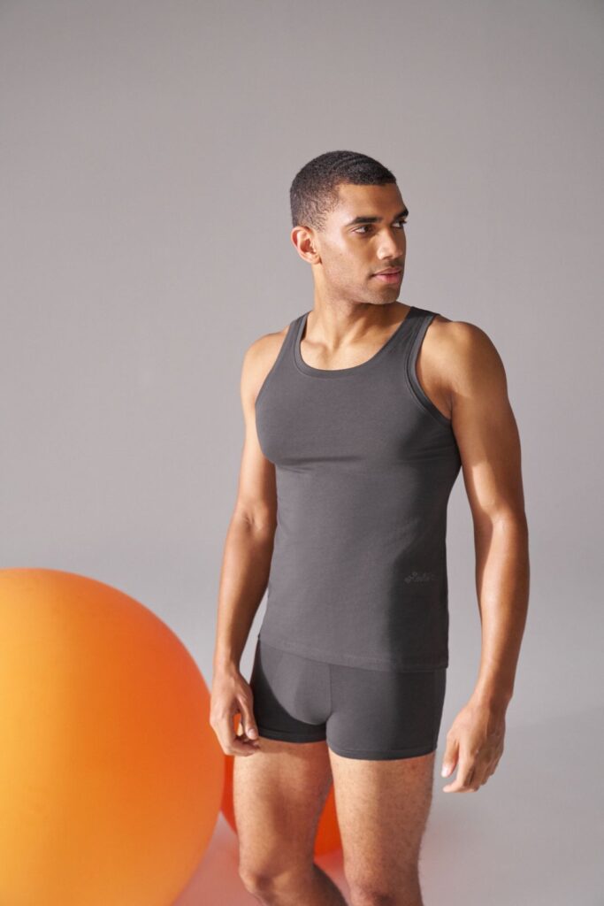 Homem em roupa interior preta, bola laranja ao fundo.