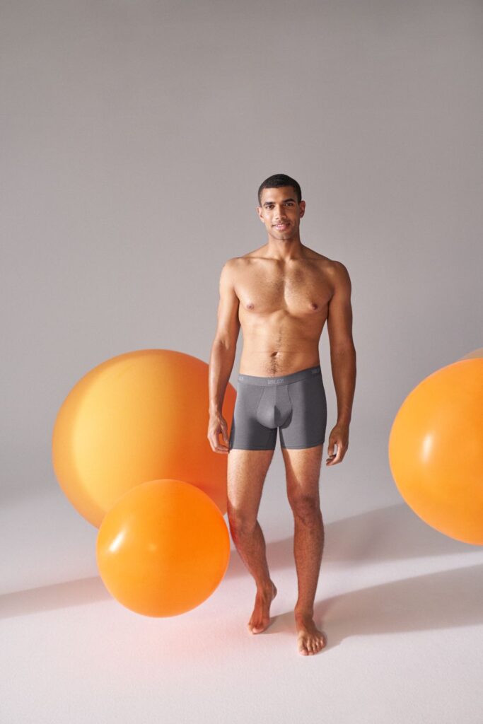 Homem em boxers cinzentos com bolas laranja ao redor.