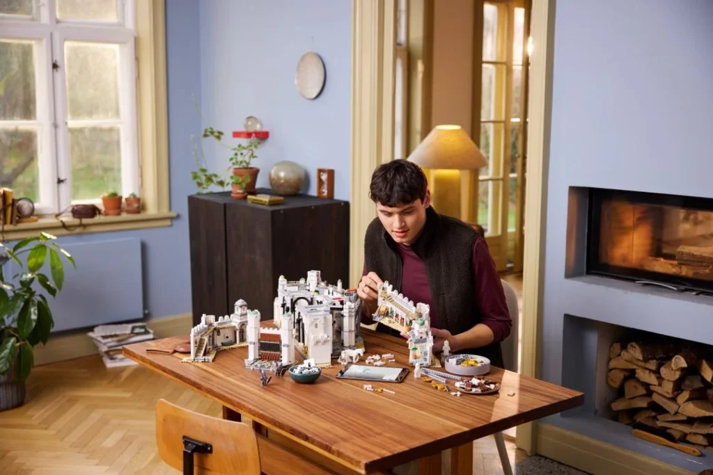 Homem a montar um grande castelo LEGO numa mesa de madeira.