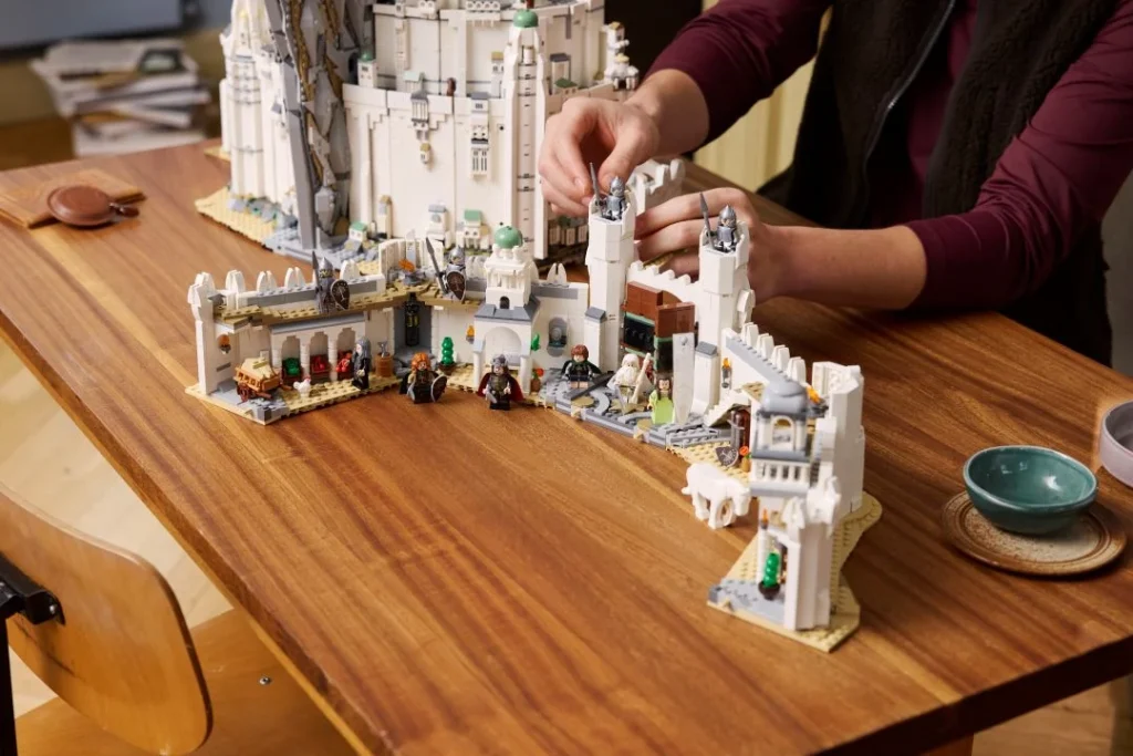Pessoa a montar conjunto LEGO Minas Tirith em mesa de madeira.