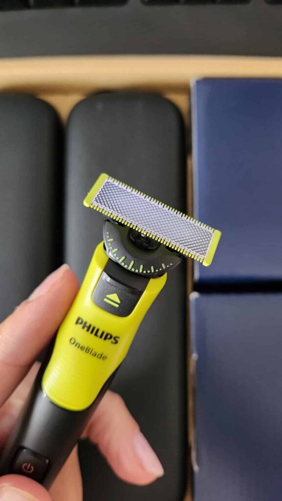 Mão a segurar uma máquina elétrica para barbear Philips OneBlade preta e verde com grelha de corte.