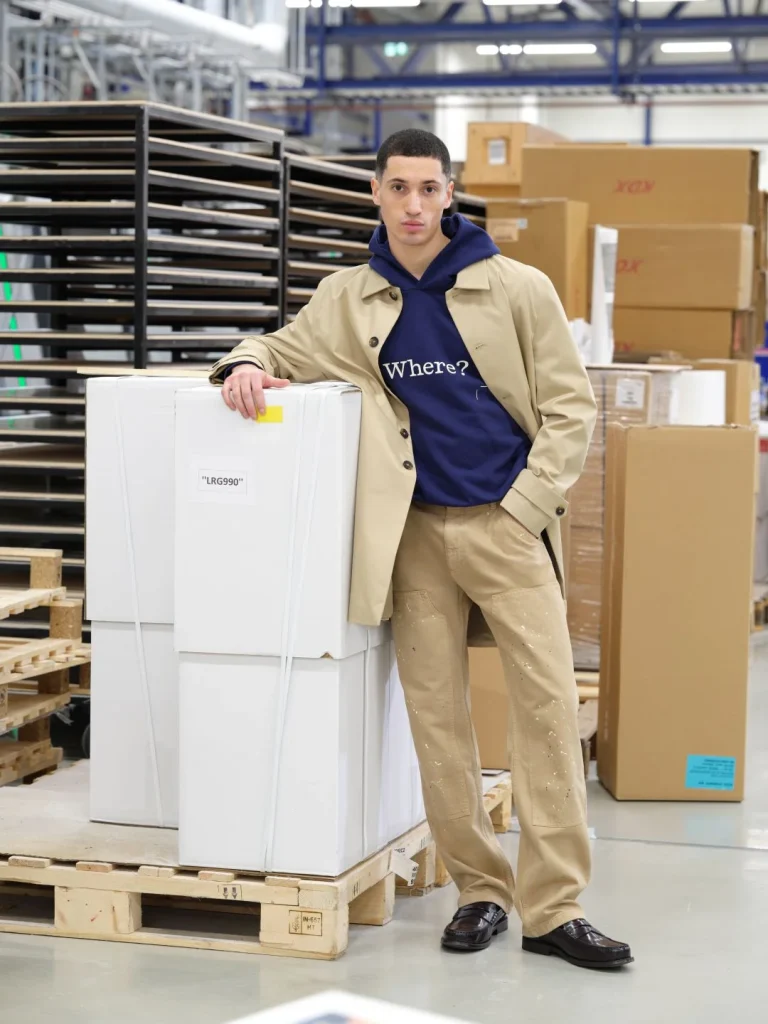 Homem com casaco bege e hoodie azul em armazém.