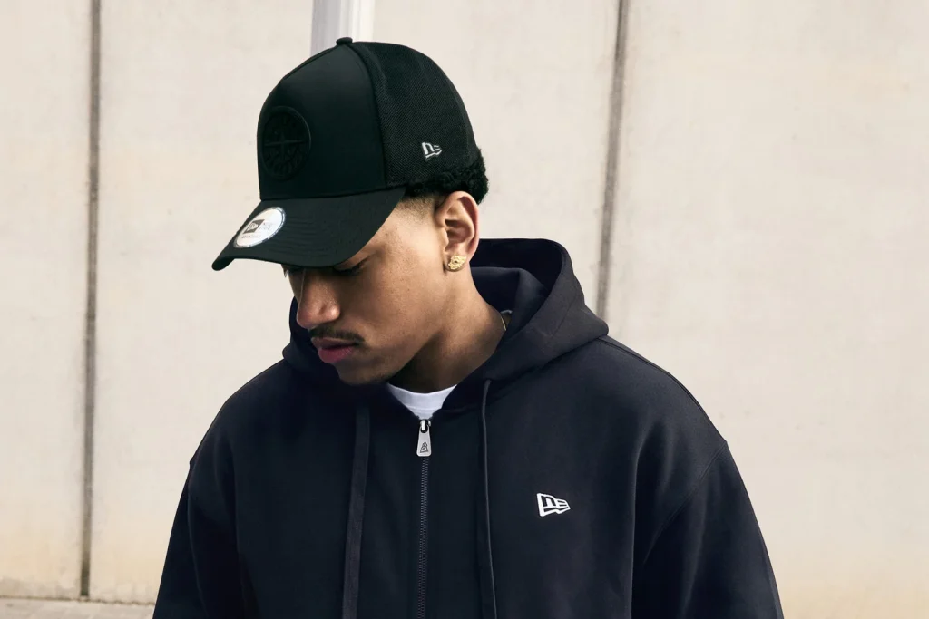 Homem com boné e casaco com capuz preto New Era.