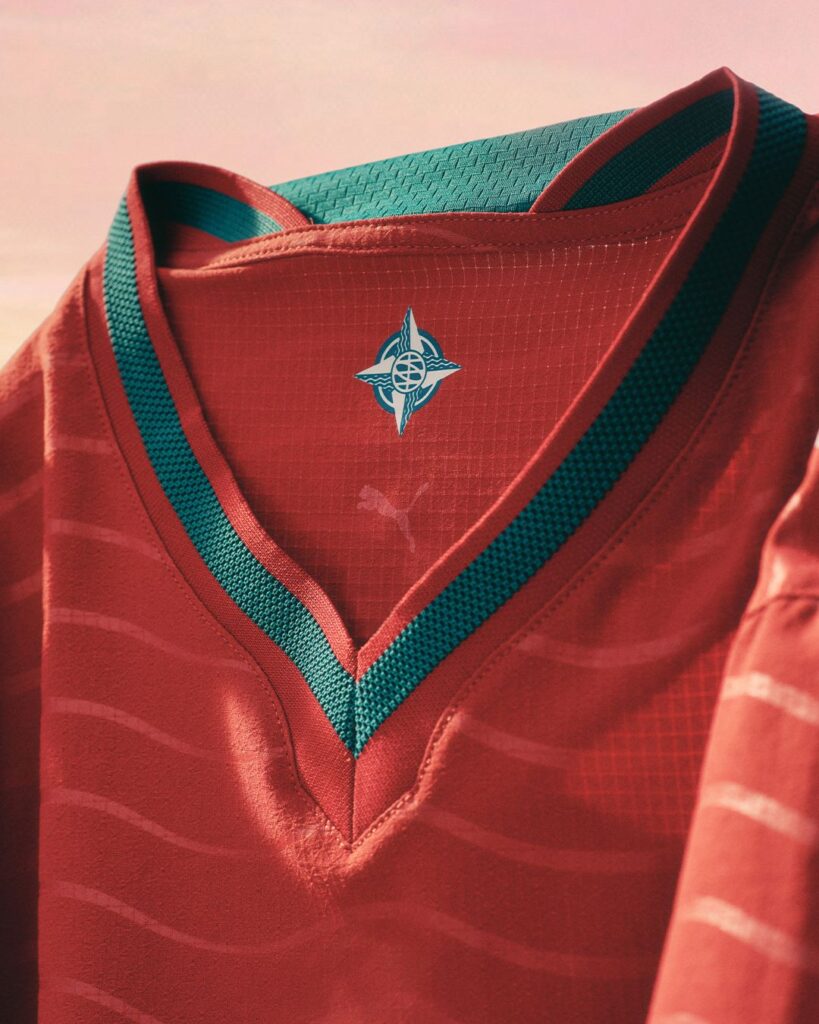 Camisola vermelha com detalhes verdes e logo central.