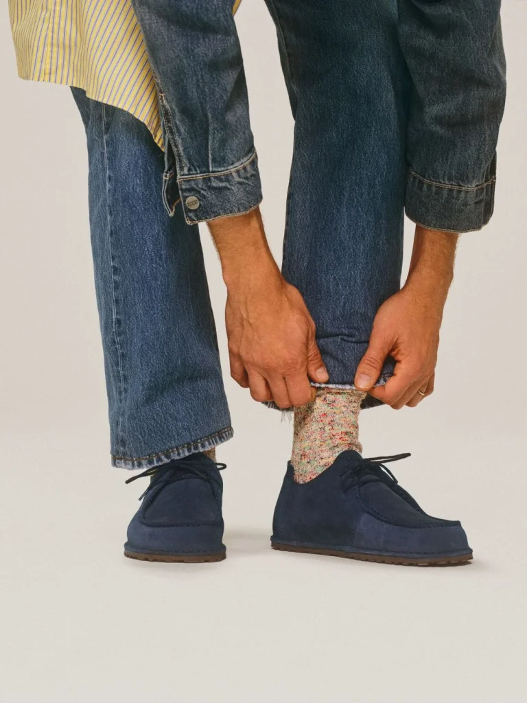 Homem a enrolar calças mostrando meias e sapatos.