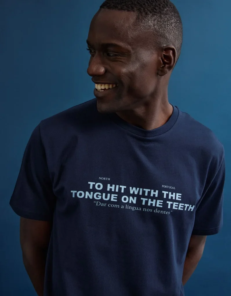 Homem sorridente com t-shirt azul, expressão portuguesa original.