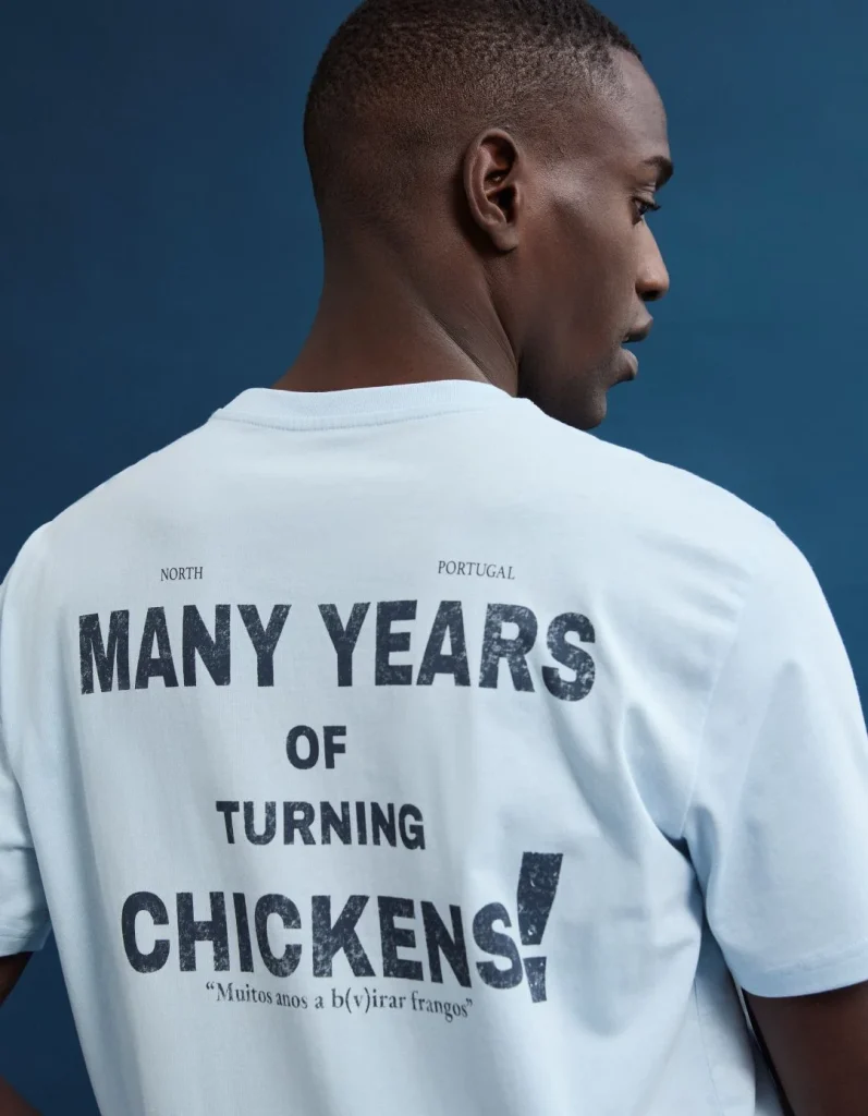 Homem com t-shirt 'Many Years of Turning Chickens' nas costas.