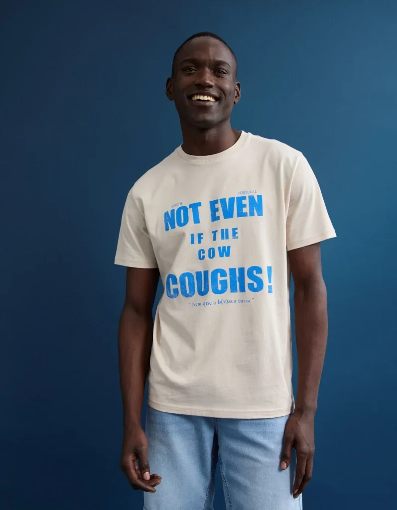 Homem sorridente com t-shirt 'Nem que a vaca tussa!'.