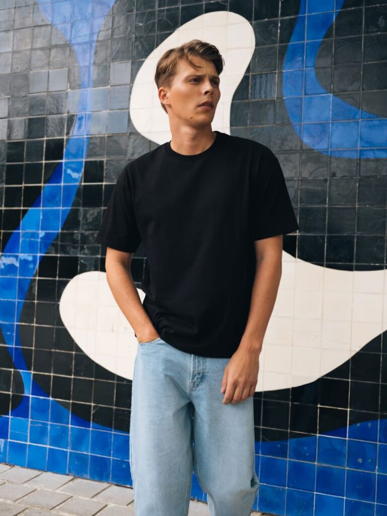 Homem com t-shirt preta e jeans casual frente a mural.