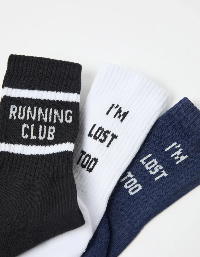 Três pares de meias com mensagens divertidas em fundo branco.