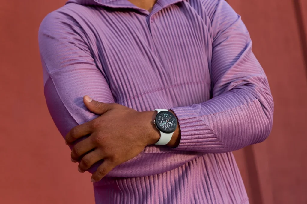 Homem com braços cruzados a usar um smartwatch branco.
