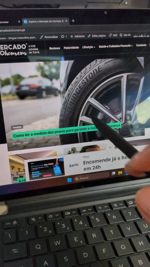 Mão a utilizar a caneta digital no ecrã tátil do portátil Asus ProArt PZ14 exibindo um artigo do blogue Mercado do Homem.