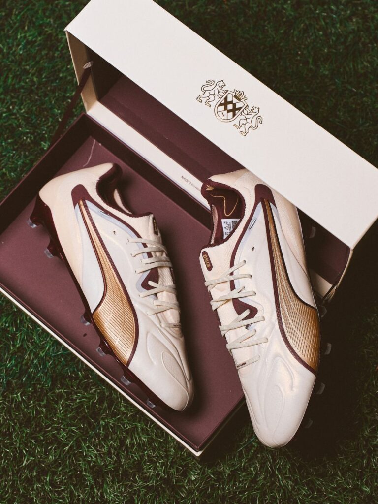 Chuteiras brancas e douradas em relva verde.