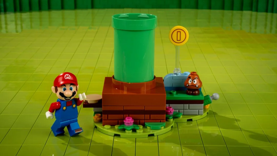 Figura LEGO Mario ao lado de um cano verde.