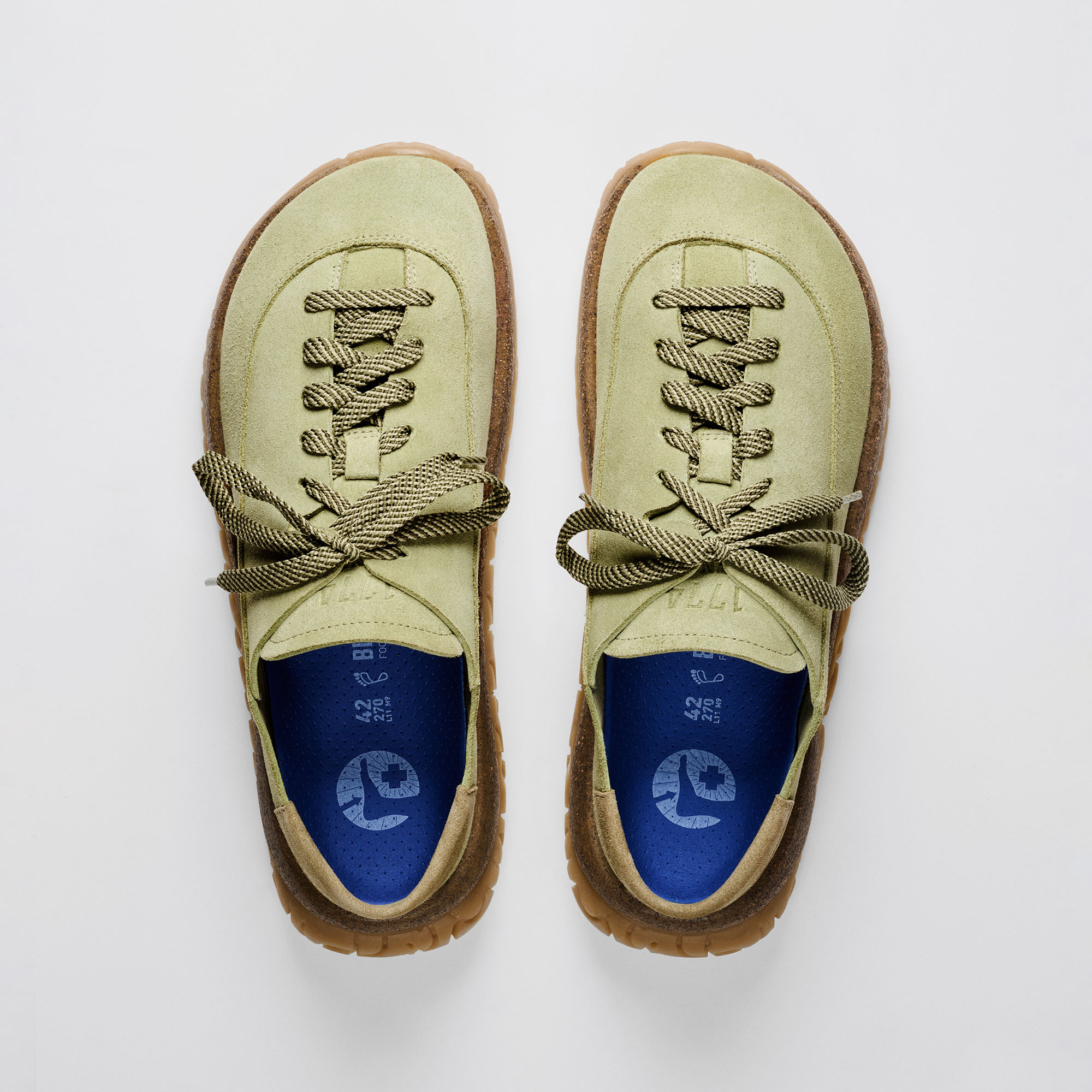 Par de sapatos híbridos Birkenstock 1774 Uerzell em camurça verde com atacadores, palmilha azul e entressola de cortiça sobre fundo branco.