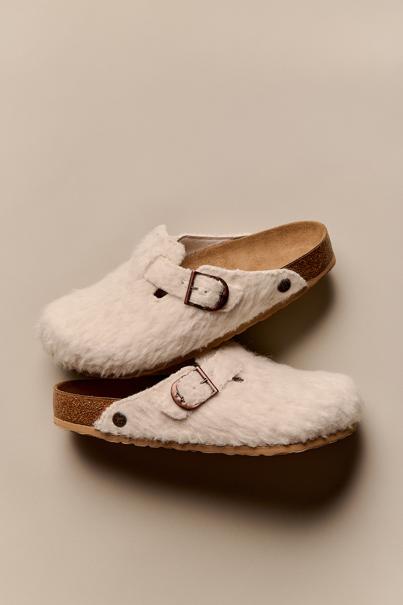 Par de socas Birkenstock Boston Cole Bennett em feltro de lã off-white com fivela de cobre sobre fundo bege