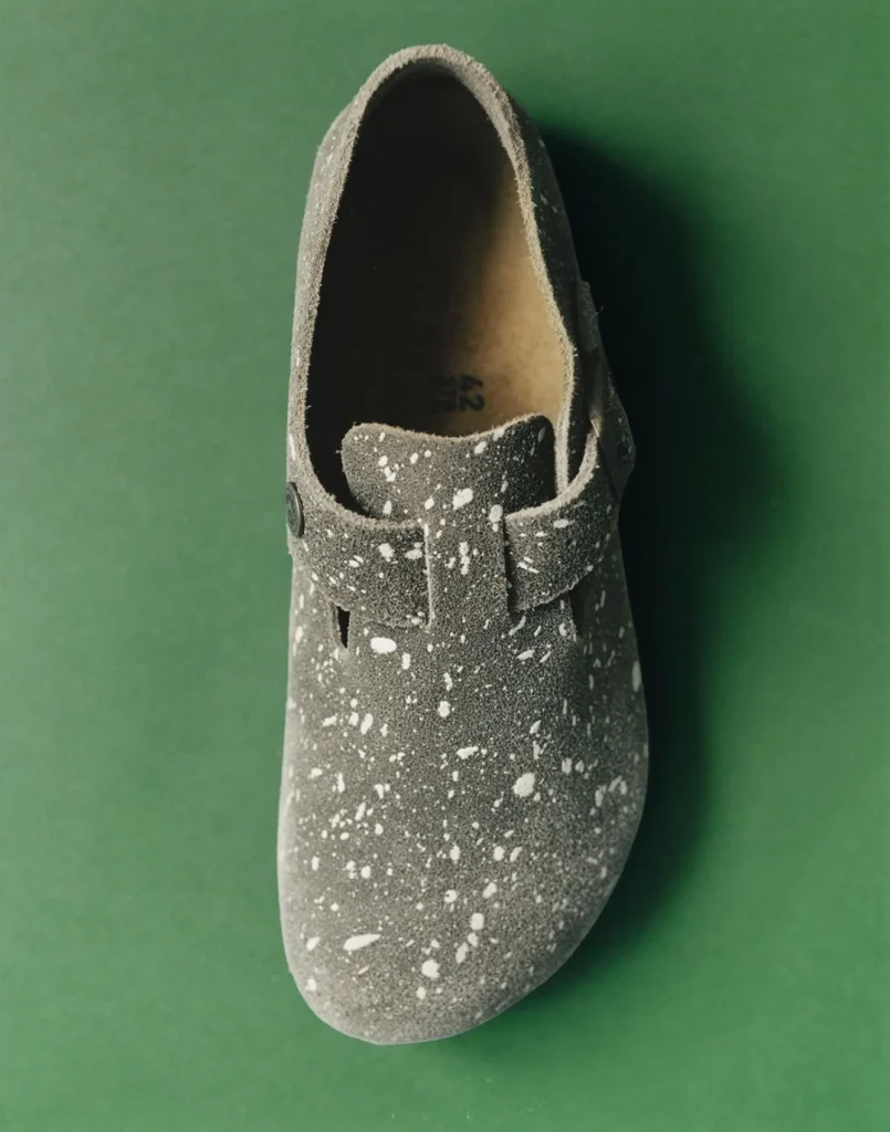 Tamanco cinzento salpicado sobre fundo verde.