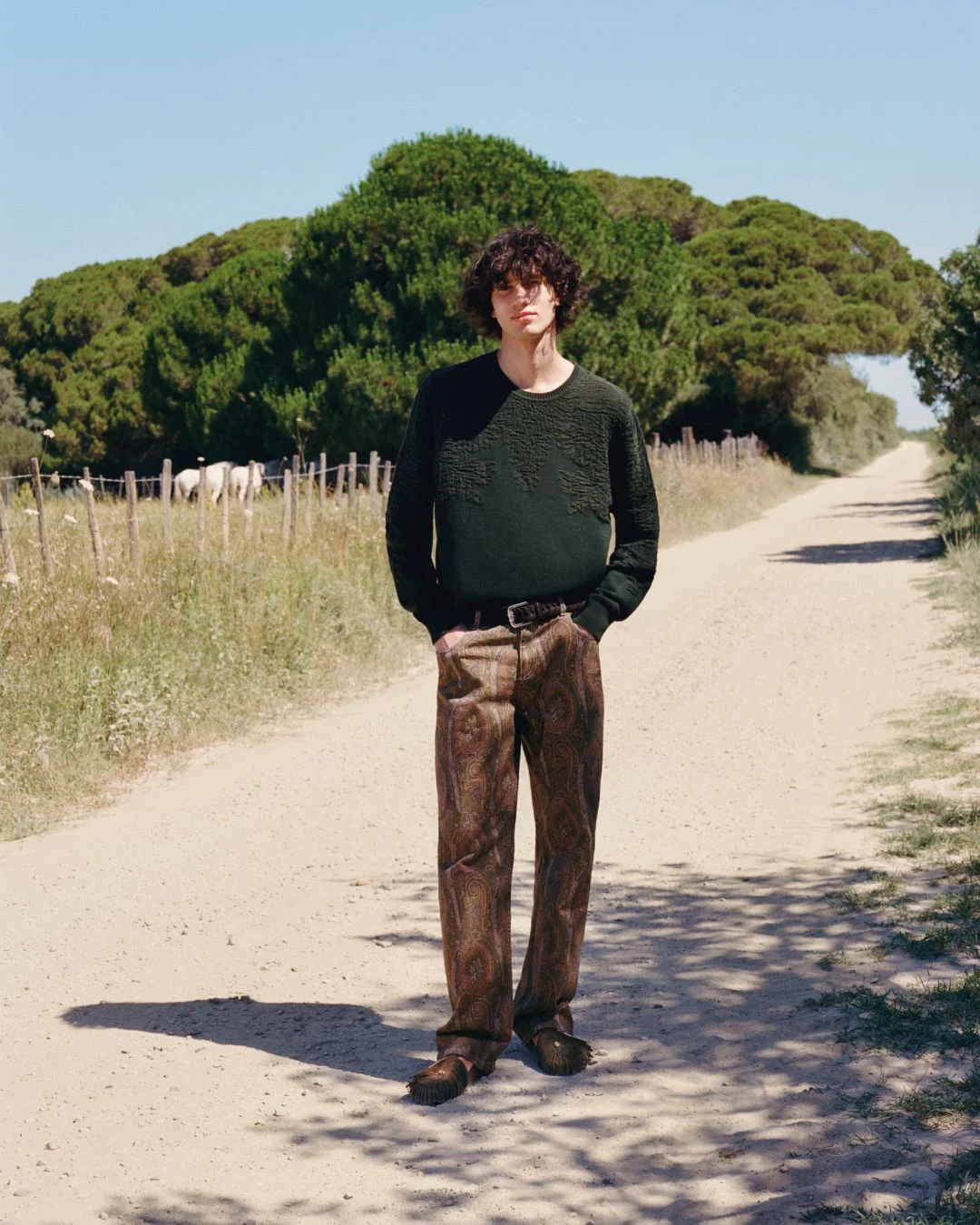 Homem num caminho de terra a vestir camisola verde escura, calças com padrão paisley e calçado Birkenstock by ETRO.