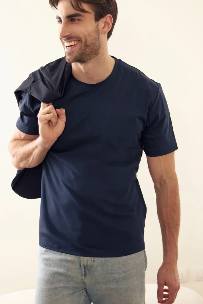 Homem sorridente com t-shirt azul-marinho e casaco ao ombro.