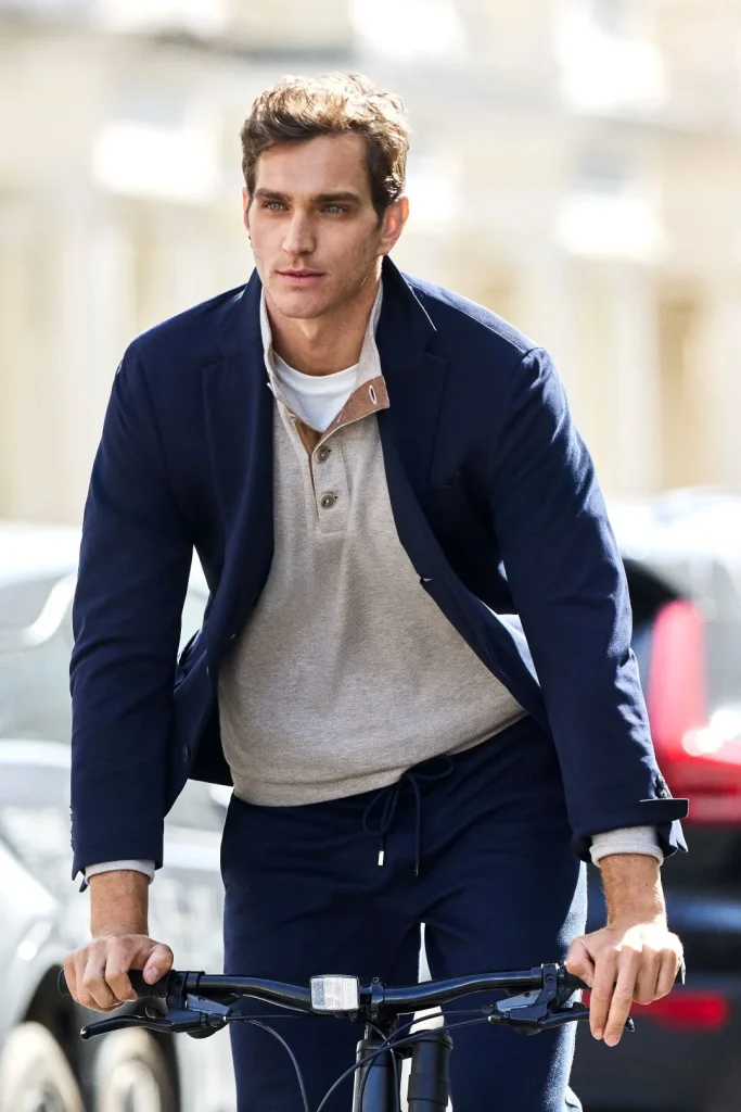 Homem a andar de bicicleta na cidade a vestir blazer azul-marinho e polo bege da coleção Hackett London outono inverno.