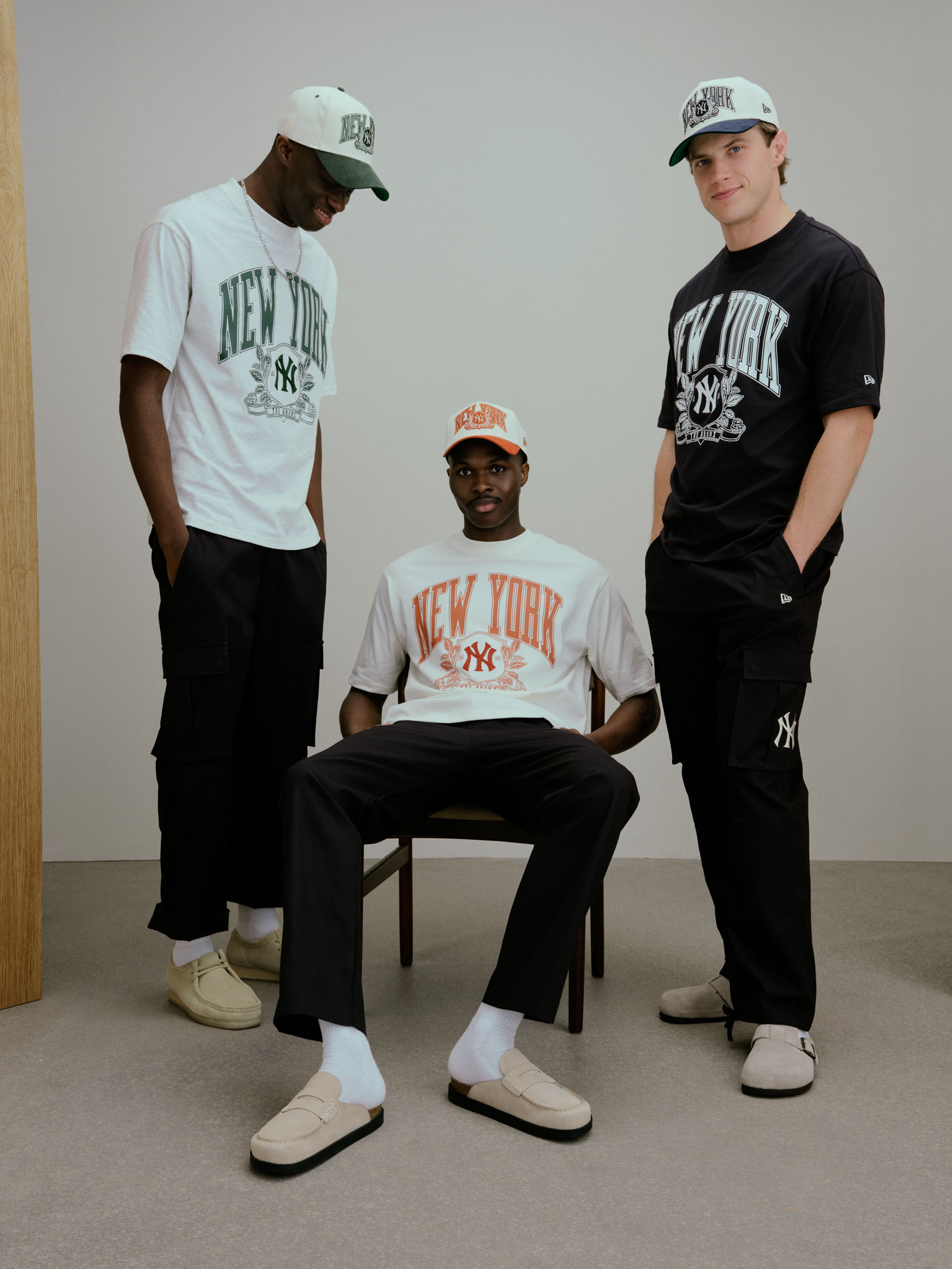 Três modelos masculinos exibem t-shirts oversized com o logótipo New York e bonés 9FORTY da coleção New Era MLB New York Yankees Clubhouse.