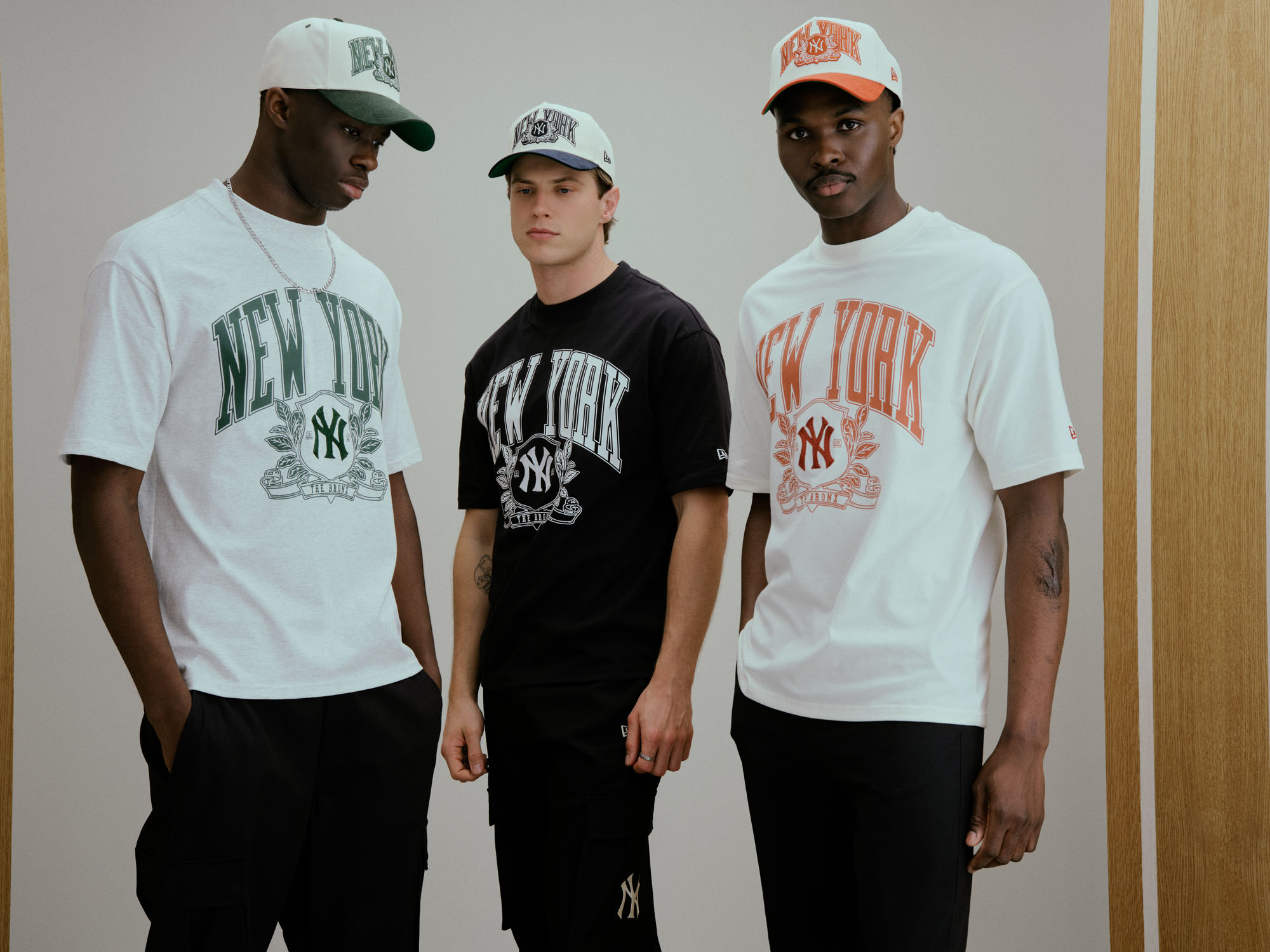 Três modelos masculinos vestem t-shirts oversized e bonés da coleção New Era MLB New York Yankees Clubhouse com o logótipo da equipa.