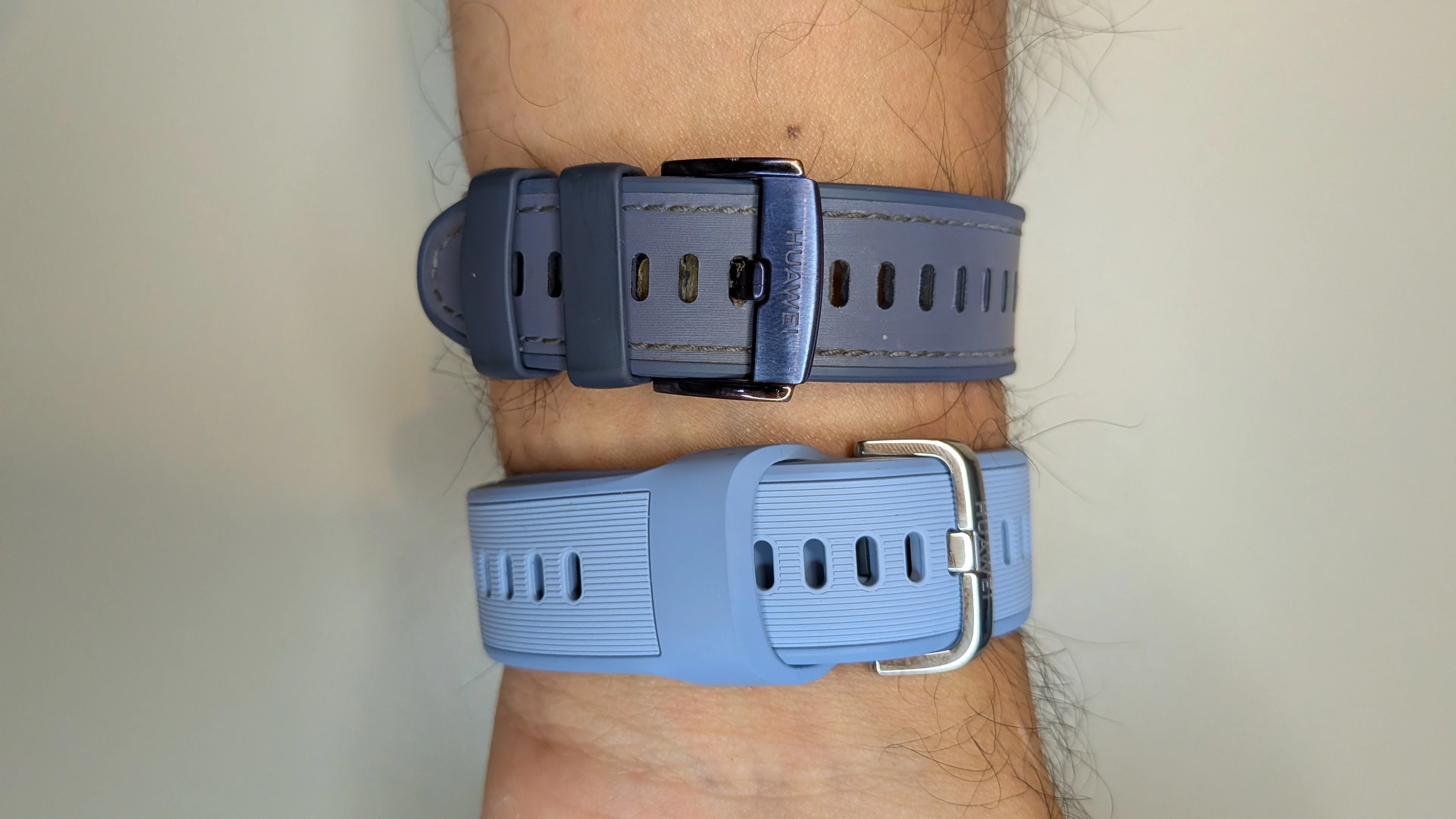 Pulso com duas braceletes de relógio lado a lado comparando o fecho tradicional escuro com a nova bracelete azul clara do Huawei Watch 6 que esconde a ponta