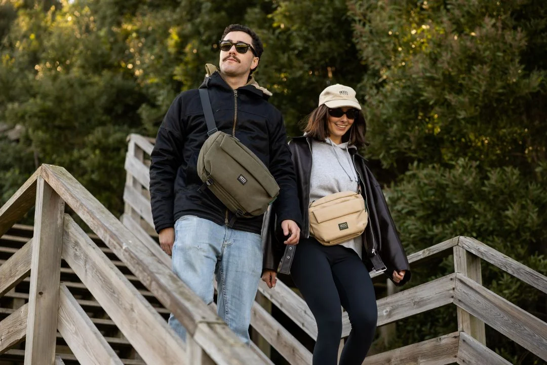 Casal com malas de tiracolo desce escadas de madeira.