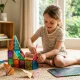 Criança a brincar com blocos magnéticos e origami no chão.