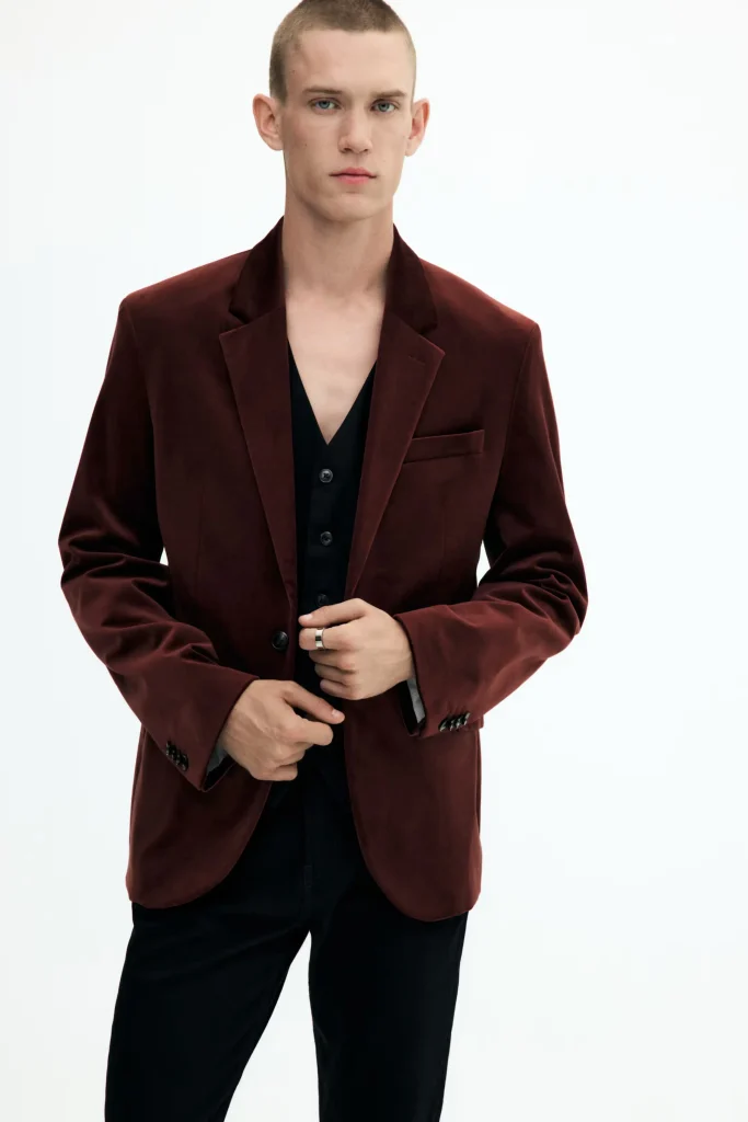 Homem com blazer vermelho escuro e colete preto.