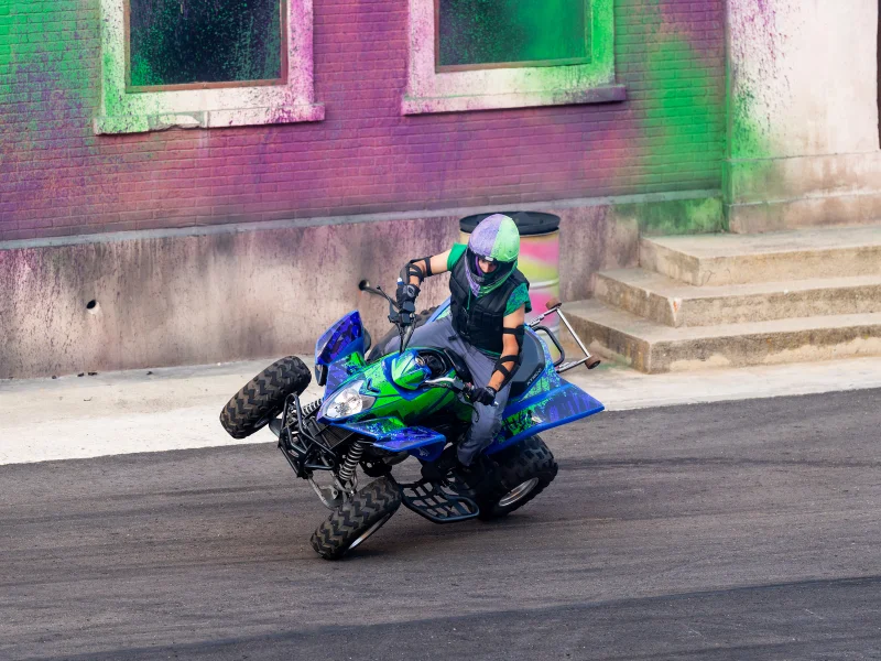 Piloto faz um cavalinho numa moto-quatro verde e azul.