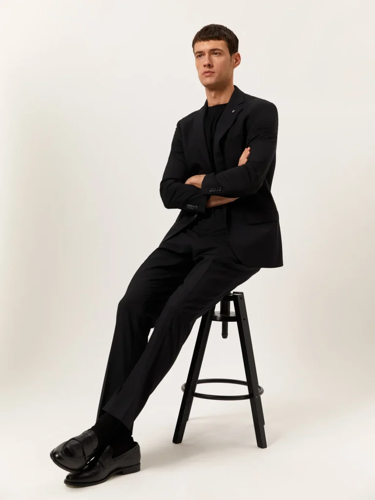 Homem sentado em banco, fato preto elegante.