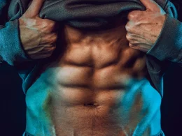 Homem a mostrar abdominais definidos sob iluminação dramática azul.