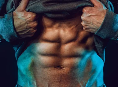 Homem a mostrar abdominais definidos sob iluminação dramática azul.