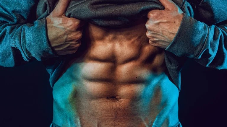 Homem a mostrar abdominais definidos sob iluminação dramática azul.