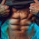 Homem a mostrar abdominais definidos sob iluminação dramática azul.