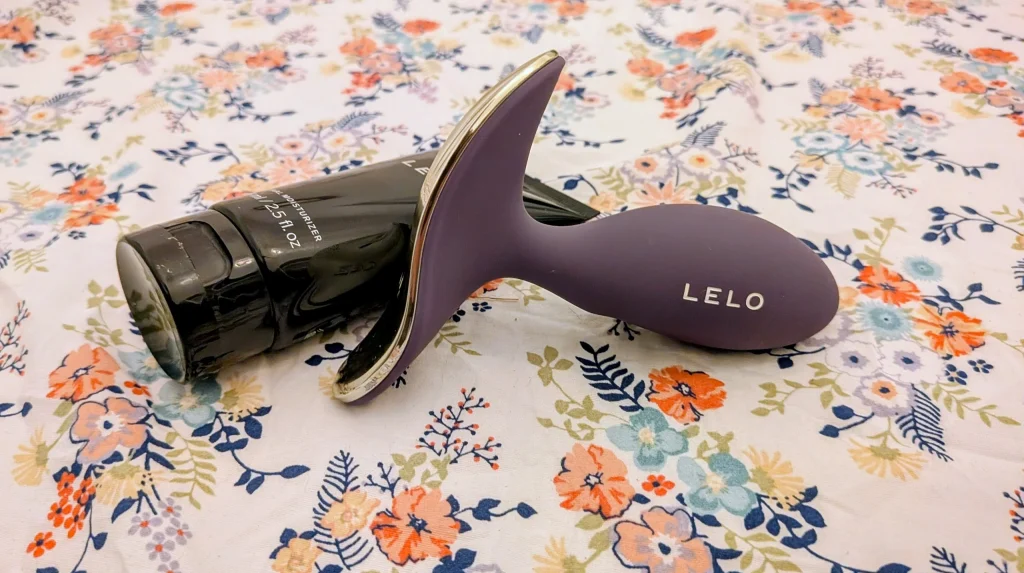 Dispositivo LELO roxo e hidratante pessoal sobre padrão floral.