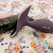 Dispositivo LELO roxo e hidratante pessoal sobre padrão floral.