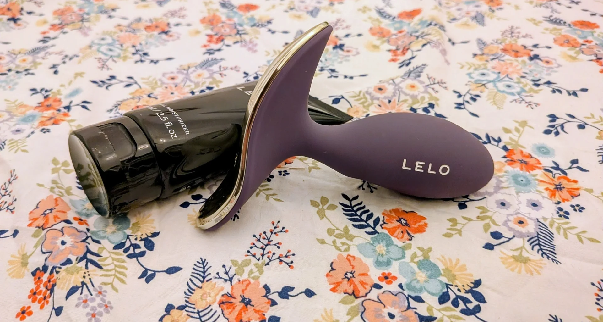 Dispositivo LELO roxo e hidratante pessoal sobre padrão floral.