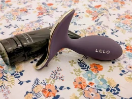 Dispositivo LELO roxo e hidratante pessoal sobre padrão floral.