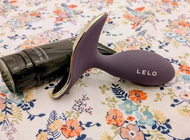 Dispositivo LELO roxo e hidratante pessoal sobre padrão floral.