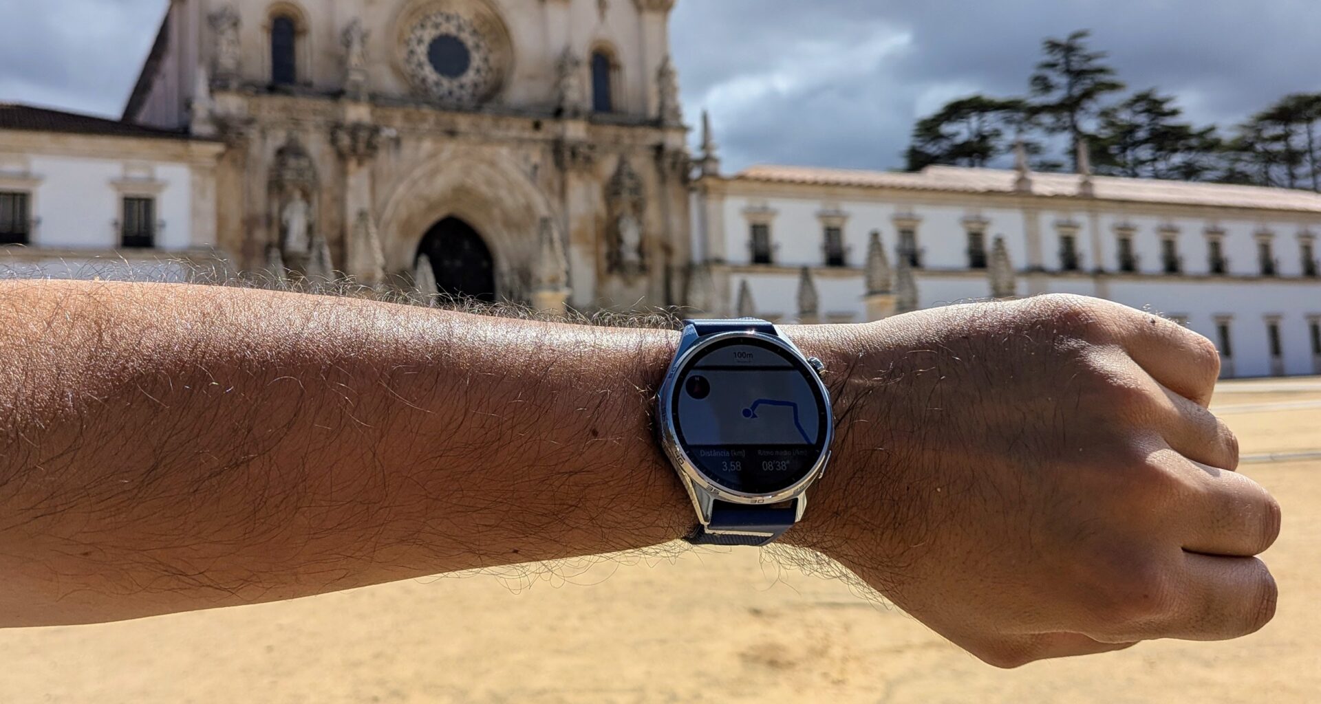 Huawei Watch GT 7 num pulso com o Mosteiro de Alcobaça ao fundo.