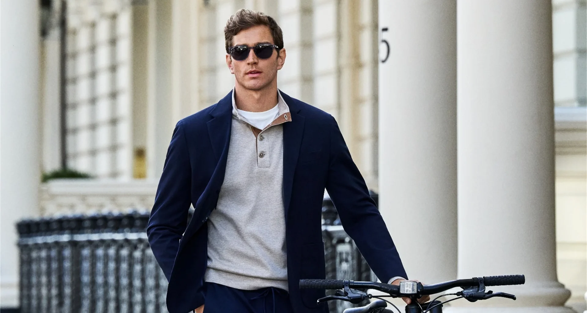Homem elegante com blazer azul e bicicleta em ambiente urbano.