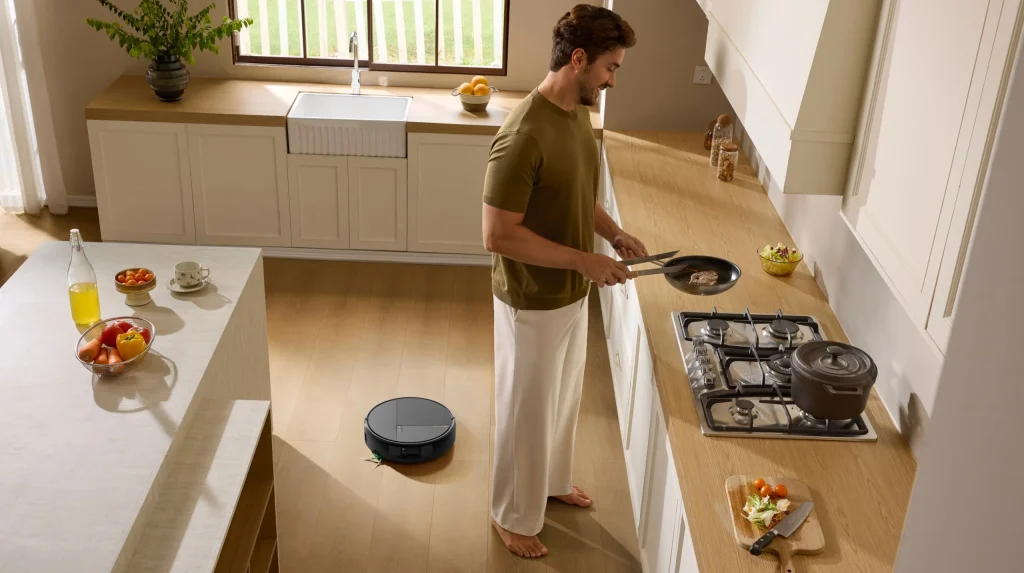 Homem a cozinhar numa cozinha moderna enquanto o aspirador robô Roomba Max 875 Combo limpa o chão de madeira