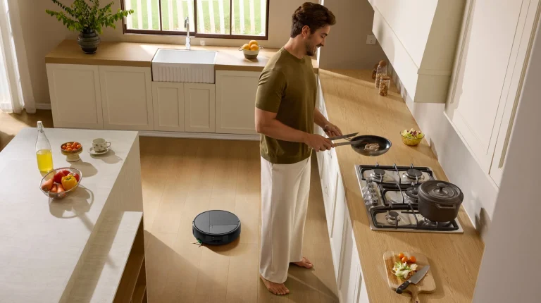Homem a cozinhar numa cozinha moderna enquanto o aspirador robô Roomba Max 875 Combo limpa o chão de madeira