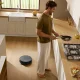 Homem a cozinhar numa cozinha moderna enquanto o aspirador robô Roomba Max 875 Combo limpa o chão de madeira
