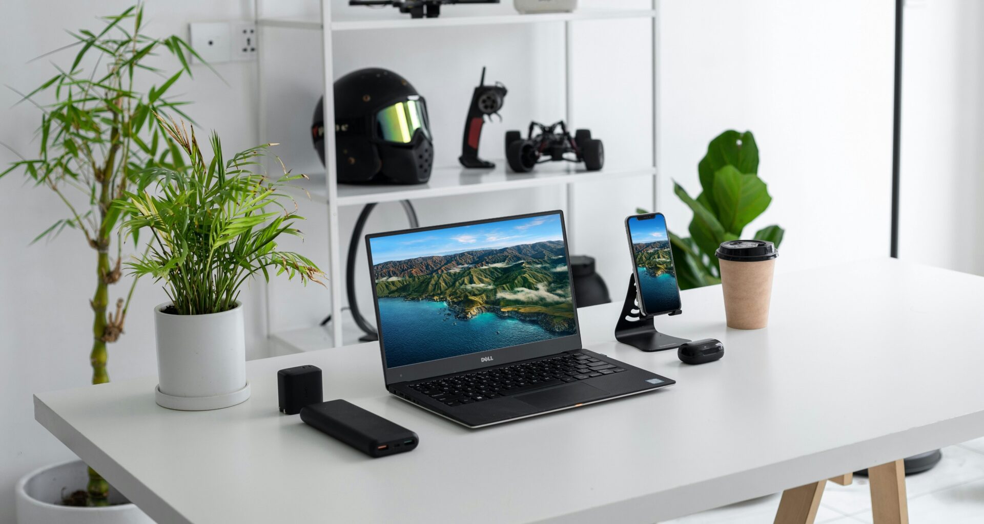 Escritório minimalista com portátil, smartphone e plantas.