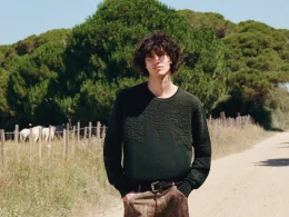 Homem com camisola verde em caminho rural com cavalos.