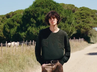 Homem com camisola verde em caminho rural com cavalos.