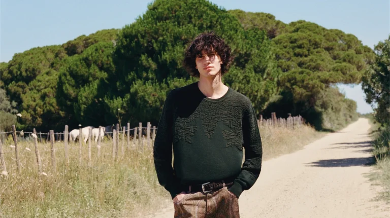 Homem com camisola verde em caminho rural com cavalos.